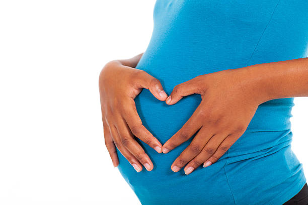 Isolated picture of pregnant African American woman active pregnant african american woman hands on belly forming a heart shape human abdomen photos stock pictures, royalty-free photos & images