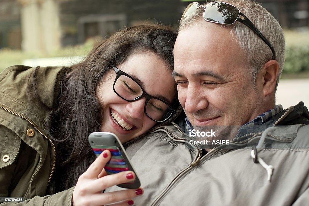 Funny moments with dad Father and teenage daughter with head in his shoulder sharing something funny in a mobile phone Father Stock Photo