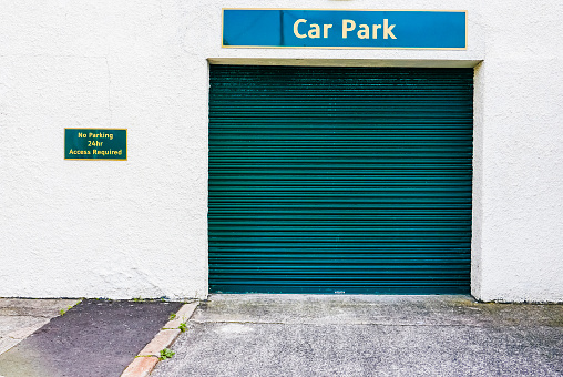 Green metal shutter at the entrance to a car park with a sign advising motorists not to park - 24 hour access required