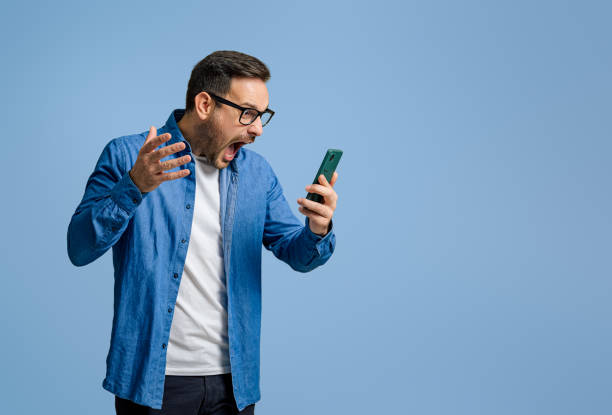 istock Male professional screaming furiously while reading message over smart phone on blue background 1787565515