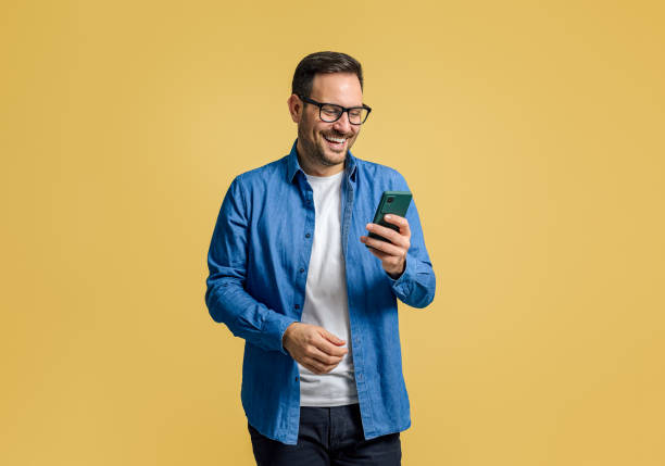 istock Happy handsome businessman online messaging over smart phone while standing on yellow background 1787565527