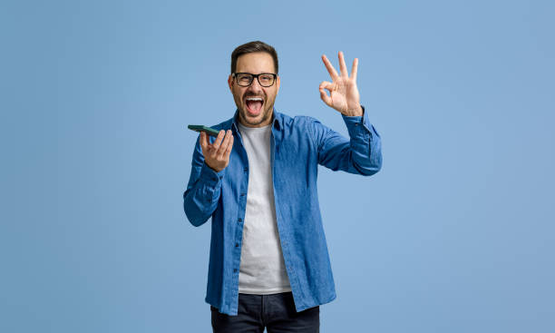istock Businessman screaming ecstatically and showing OK sign while using cellphone on blue background 1787566557