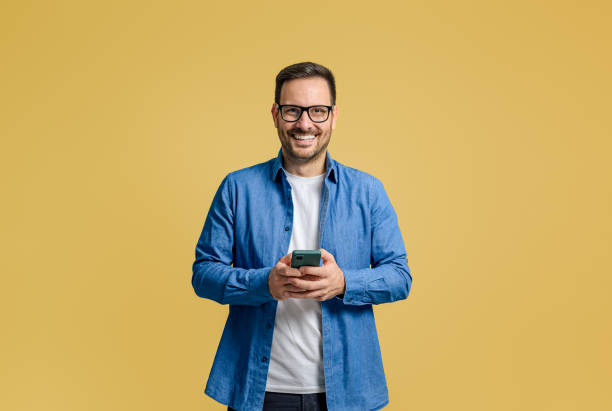 istock Smiling male professional texting over cellphone while standing confidently on yellow background 1787566568