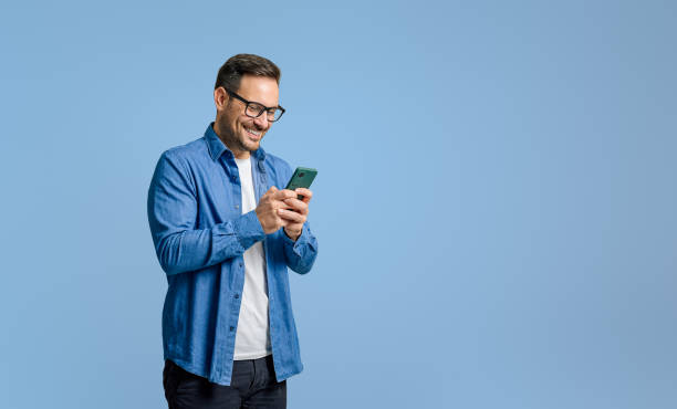istock Smiling handsome businessman text messaging over mobile phone while standing on blue background 1787566569