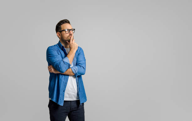 Young male entrepreneur with hand on chin thinking business ideas while standing on white background