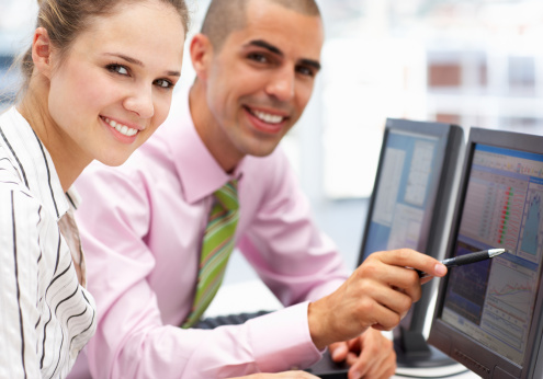 Businessman and woman working on computers in office smiling to camera