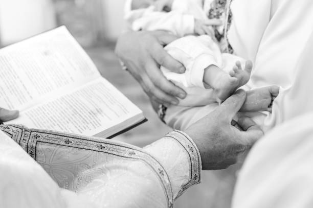 The priest performs the rite of baptism of the child and anoints the leg with holy peace. The priest performs the rite of baptism of the child and anoints the leg with holy myrrh, the sacrament of Christian baptism. pics of the godmother stock pictures, royalty-free photos & images