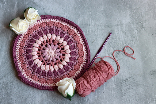 Crocheted trivet made of pink organic yarn. Handmade crochet potholder on gray background with space for text.