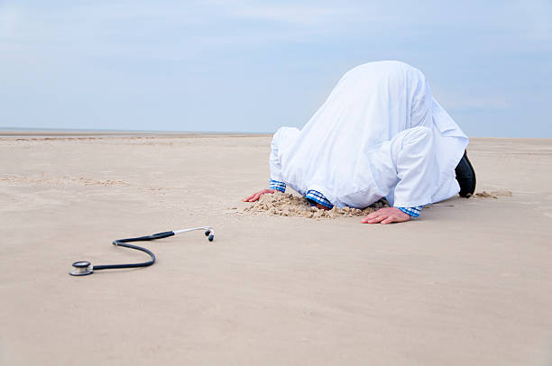 Doctor hiding head in sand stock photo