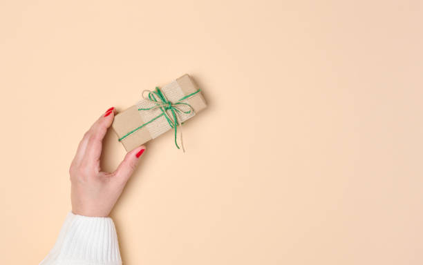 istock Female hand holding a gift box on a beige background. View from above 1787661967