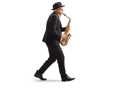 Full length profile shot of a man walkign and playing a sax isolated on white background
