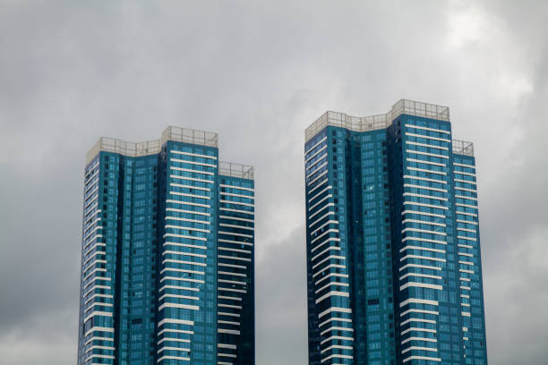 Top of two skyscrapers with massive rainclouds in the background. The buildings have a blueish color, and they look like towers for expensive city apartments or business offices. It looks like the rain can start to fall any time. The pictures was made in Busan, South Korea on an early October day.