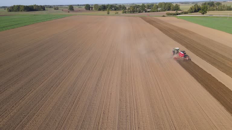 Drone sliding shot of a farmer in tractor seeding, sowing agricultural crops at field