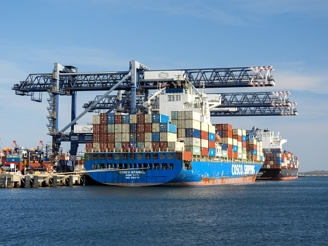 The Cosco Istanbul and the Rio Grande container ships docked at the Port Botany Container Terminal in Botany Bay, Sydney.  The ship is flying a red flag, indicating dangerous cargo. This image was taken on a sunny and windy afternoon on 11 November 2023.