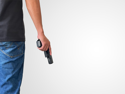 A man wearing a black short-sleeved shirt and jeans stands holding a handgun, symbolizing the killing of people, murder, Active shooting.