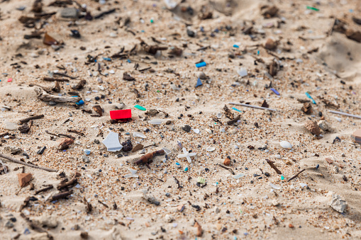 Plastic trash in sand on ocean beach. Pollution by microplastic rubbish on coastline