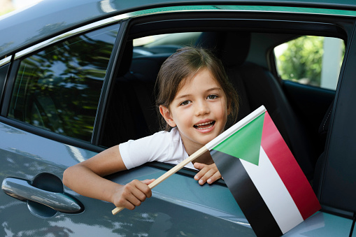 Girl in car is holding Palestinian flag with a toothy smile and is looking at camera.