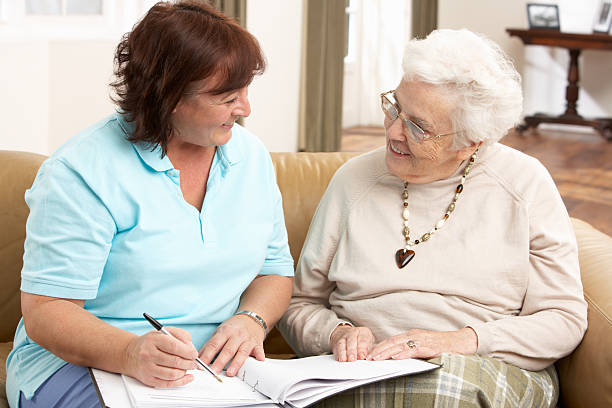 Senior Woman In Discussion With Health Visitor At Home Senior Woman In Discussion With Health Visitor At Home Writing Down Information Smiling At Each Other independence stock pictures, royalty-free photos & images