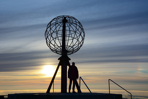 Unrecognizable tourist silhouette, midnight sun and clouds at the North Cape (norwegian: Nordkapp). North Cape is the northernmost point of Continental Europe and one of the most popular attraction in Norway