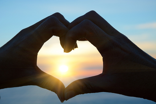 Hands formig heart shape with sunset on background