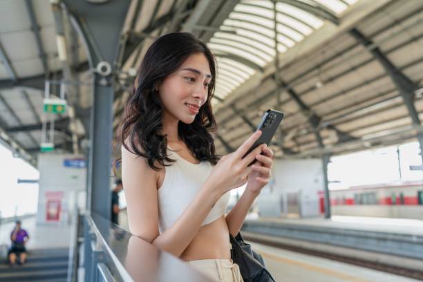 istock Young asian woman using the phone while waiting for public transport transit train at the mass transit station platform 1787718085