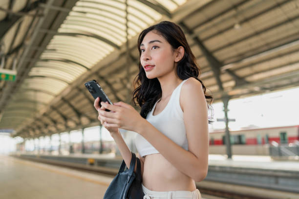 istock Young asian woman using the phone while waiting for public transport transit train at the mass transit station platform 1787719164
