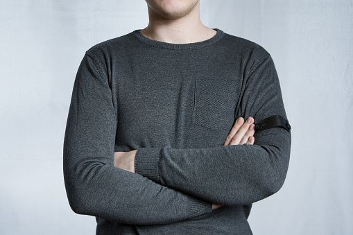 Young man folded arms across chest in gray sweater on light gray background. A sign of indifference, waiting