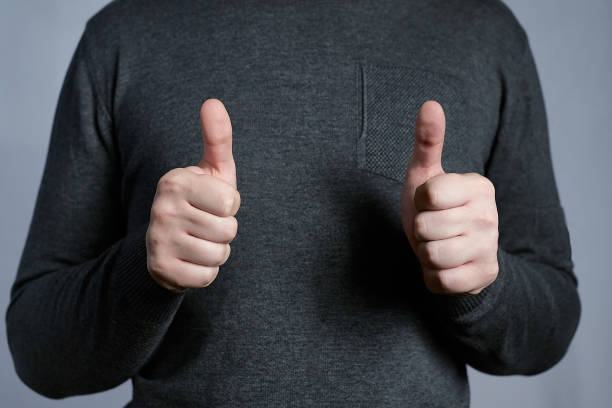 dwa kciuki w górę na obu rękach młodego mężczyzny ubranego w szary sweter na jasnoszarym tle. - endorsement appreciate validate thumbs up zdjęcia i obrazy z banku zdjęć