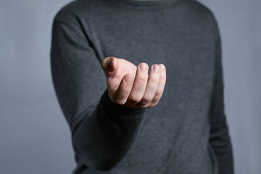 Begging hand gesture of a young man in a gray sweater. A sign asking for something, asking to give something