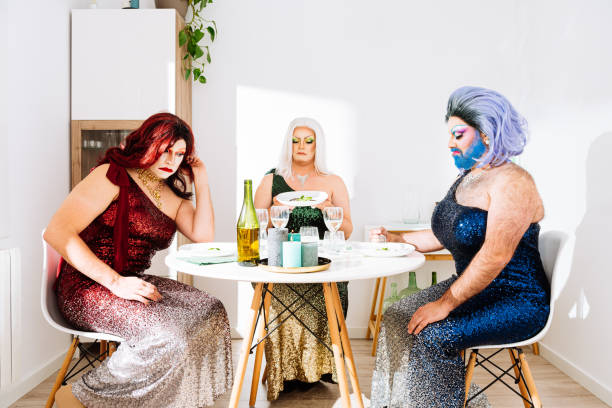 Upset drag queens looking at tasteless dishes at table Unsatisfied adult drag queens in colorful dresses with makeup and wigs sitting at table and looking at tasteless dishes during party at home gay dinner table stock pictures, royalty-free photos & images