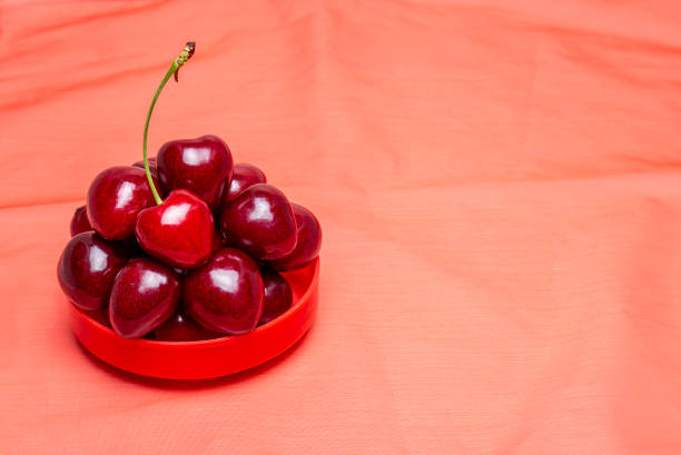 Cherries in a red bowl on a red cloth background.