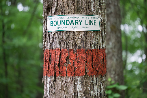 Sign on tree with trail marker for Boundary Line National Park Service