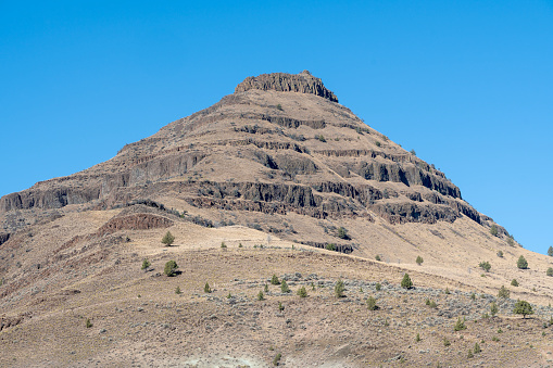 Picture Gorge Basalt showing layers of basalt lava flows with columnar jointing separated by thin layers of fossil bearing rock. Across highway OR 19 to west from Blue Basin, John Day Fossil Beds National Monument, Oregon, USA.
