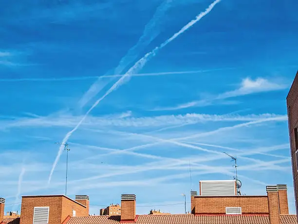 Chemtrails on blue sky over city buildings
