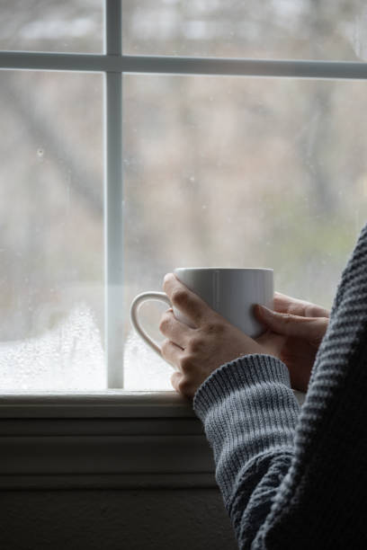 istock hands holding cup in front of window with snow 1787861310