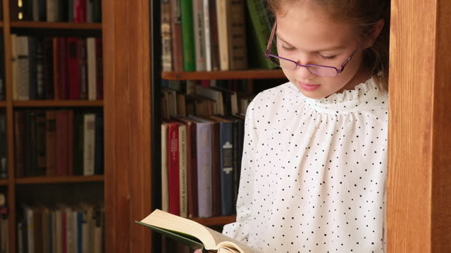Kid girl in glasses reading book in old public library. Schoolgirl in bookstore