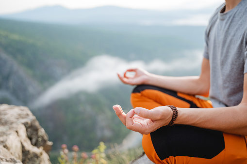 A yogi sits in the lotus position on top of a mountain. A fragment of a part of the human body in a posture of relaxation and immersion in meditation in nature, Zen in the mountains.