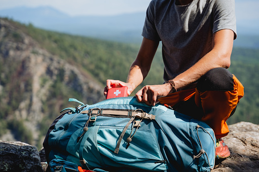 Take out a first aid kit from the pocket of a backpack, a red mini bag with medicines, a first aid kit on a trip, a hand pulls a bag with medicines. High quality photo