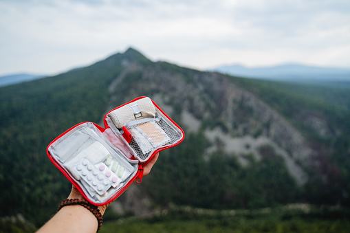 Tourist equipment first aid kit, hand holds an open first aid kit, a set of pills, self-help in a hike, mountain top. High quality photo