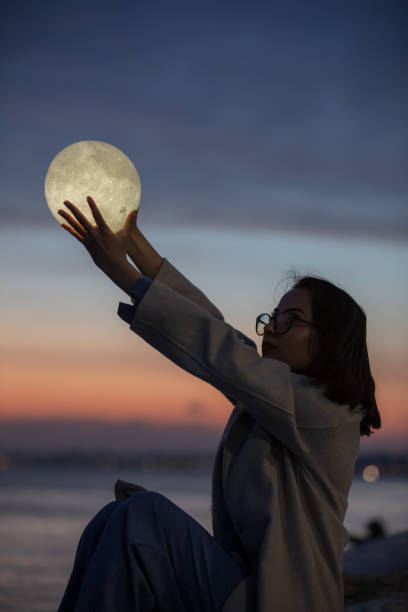 istock Pretty young woman is playing with a moon shaped artificial lamp at sunset. 1787897283