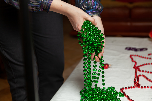 Woman hands laying a long green garland of small balls on a white table close-up