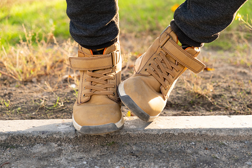 Feet of a little boy in brown nubuck shoes in autumn in a city park. Comfortable waterproof demi-season shoes.