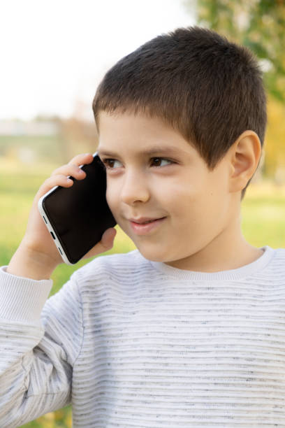 istock Handsome 6 year old boy talking on the phone while standing in park in autumn. 1787933984