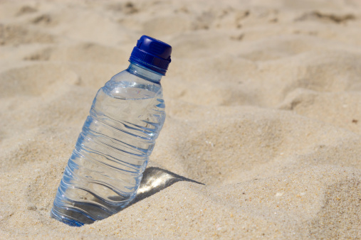 Photo of a water bottle on the sand at the beach.