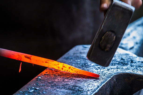 blacksmith's hammer working a heated metal rod on an anvil - aambeeld stockfoto's en -beelden