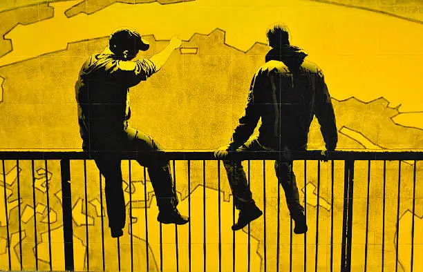 Photo of European graffiti showing two boys sitting on fence.