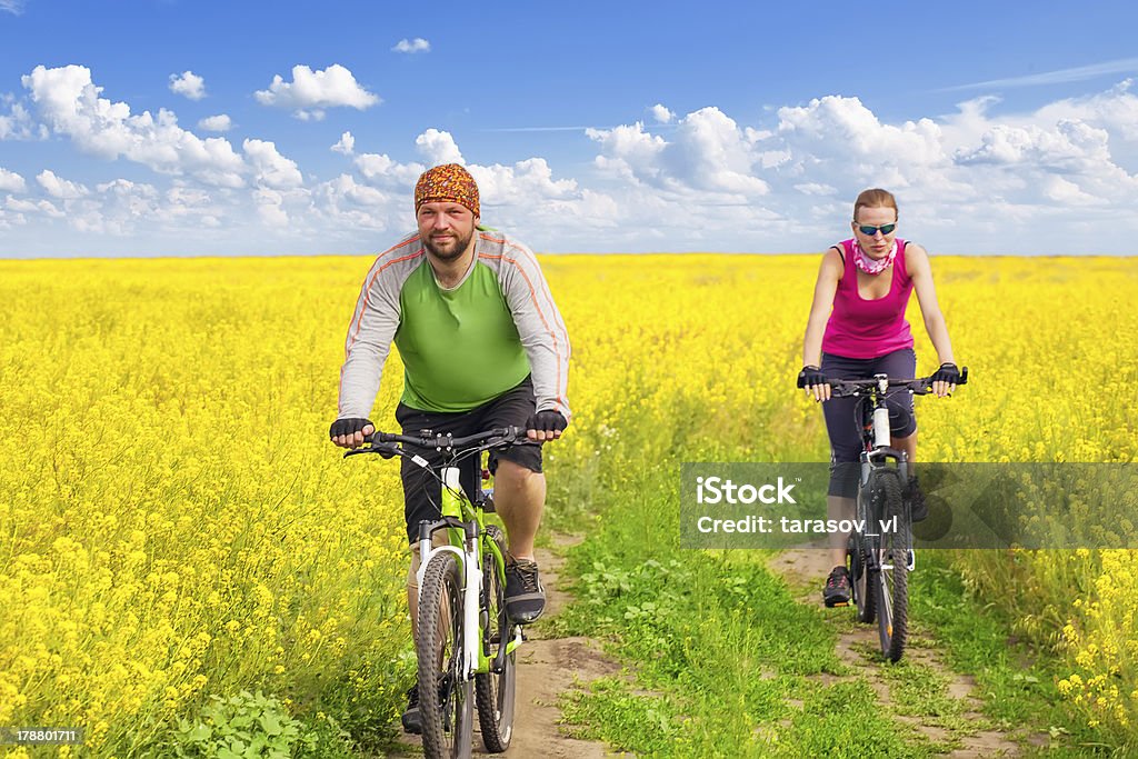 Casal feliz ciclismo em campos de canola - Foto de stock de Adulto royalty-free