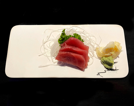 Tuna sashimi with wasabi, ginger, rice noodles and soy reduction on a black background