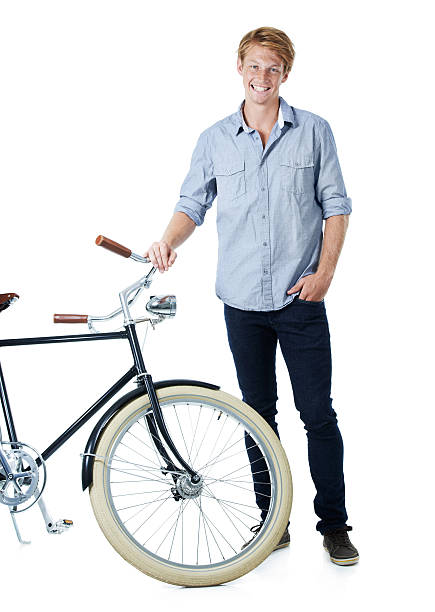 A smiling young red-headed man standing next to an old-fashioned bicycle with his hands in his pockets