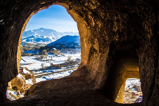 A large, rocky cave entrance opens up to a stunning view of the snow-capped mountains beyond